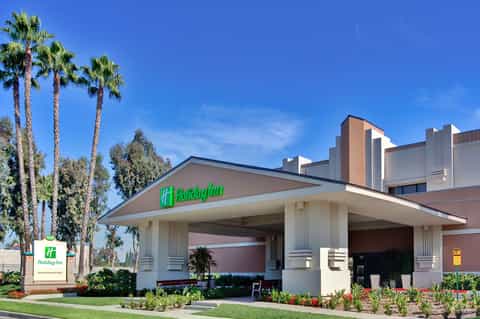 Holiday Inn hotel entrance with palm trees, white columns, and green neon signage