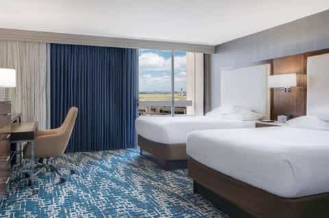 Hotel twin bedroom with blue curtains, city view, and contemporary furnishings