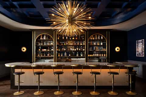 Upscale bar with gold sunburst chandelier, dark walls, and arched bottle displays