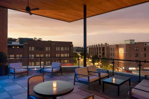 Urban rooftop lounge at dusk with blue chairs, fire pit, and city skyline views