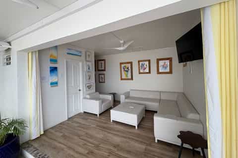 Bright living room with light gray sectional sofa, framed artwork, television, and yellow curtains