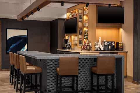 Contemporary home bar with dark cabinetry, brass accents, leather bar stools, and stocked shelving