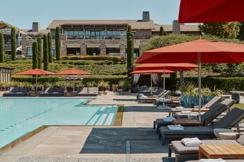 Resort pool with red umbrellas, lounge chairs, stone building, and manicured landscaping