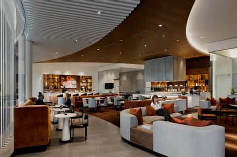 Contemporary hotel lobby lounge with curved seating, wood ceiling, bar area, and ambient lighting
