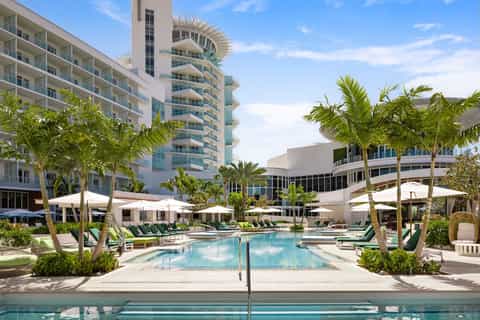 Resort pool surrounded by palm trees, lounge chairs, and modern hotel buildings
