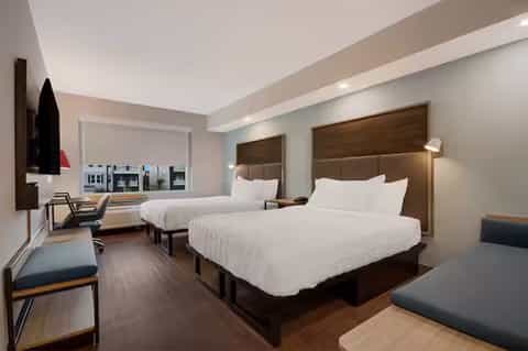 Modern hotel room with two queen beds, brown headboards, desk area, and contemporary furnishings