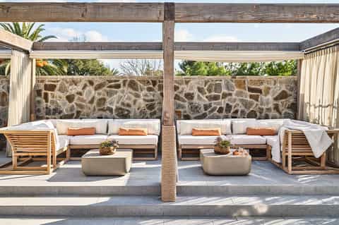 Outdoor seating area with cream cushioned sofas, wooden furniture, and stone accent wall