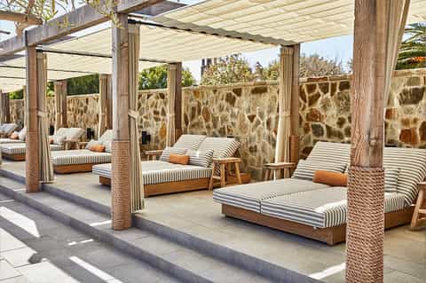Poolside loungers under wooden pergola with striped cushions and stone walls