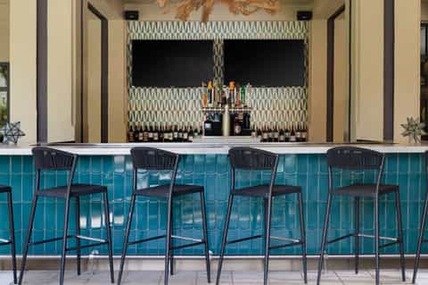 Upscale bar with teal tile accents, black bar stools, patterned wallpaper, and professional liquor display