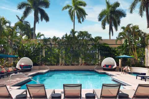 Resort pool with turquoise water, white dome cabanas, palm trees, and lounge seating