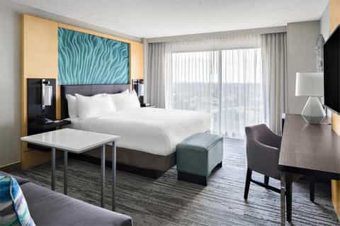 Contemporary hotel bedroom with king bed, turquoise headboard art, balcony view, and modern furnishings