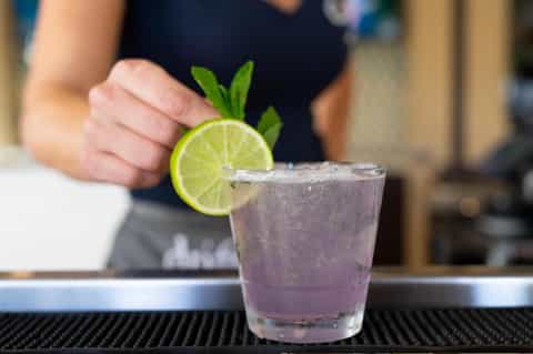 Bartender garnishing cocktail with lime slice and mint on bar counter