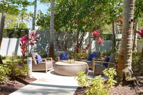 Outdoor lounge seating with curved furniture, tropical plants, and red flowers under trees