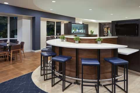 Modern hotel bar with curved white countertop, dark wood base, and blue bar stools