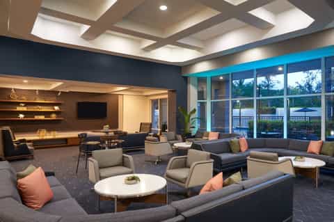 Modern hotel lounge with gray seating, coral pillows, and large windows