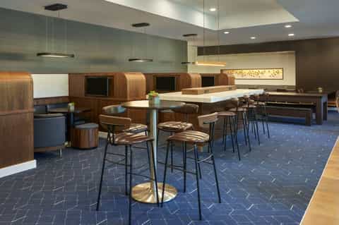 Modern hotel lounge with wooden booth seating, bar counter, and contemporary pendant lighting