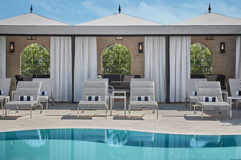 Modern pool cabanas with white umbrellas and striped lounge chairs facing a tranquil blue pool