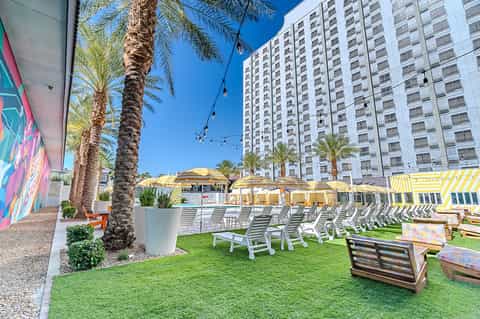 Resort courtyard with green lawn, white lounge chairs, yellow umbrellas, palm trees, and buildings