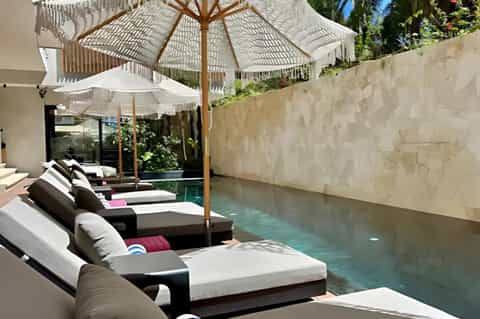Infinity pool with black lounge chairs, white umbrellas, and modern architecture against stone wall