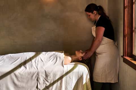 Spa therapist performing massage treatment on client lying on bed in spa room