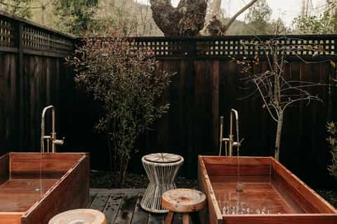 Two wooden soaking tubs on wooden deck with plants and dark fence in spa or wellness area