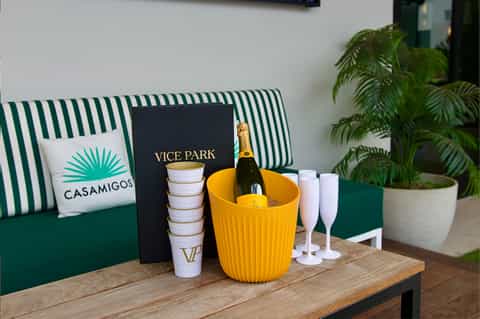 Vice Park branding with champagne bottle in yellow bucket, green striped seating, and palm plant accents