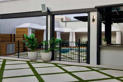 Contemporary patio with black steel pergola, white curtains, potted plants, and pool view beyond glass doors