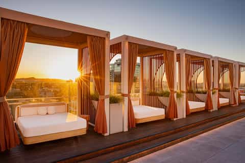 Rooftop cabanas with copper-colored frames and white bedding at sunset with city views