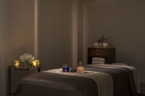 Spa treatment room with two massage tables, candlelight, flowers, and skincare products