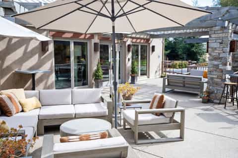 Rooftop terrace with lounge seating, large umbrellas, and stone accent wall overlooking residential area
