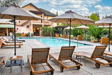 Upscale resort pool area with wooden lounge chairs, umbrellas, and Spanish-style building