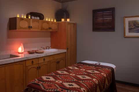 Spa treatment room with wooden cabinetry, massage table with geometric blanket, and warm ambient lighting