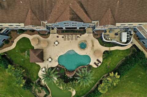 Aerial view of resort with curved pool, landscaped grounds, and surrounding brick buildings