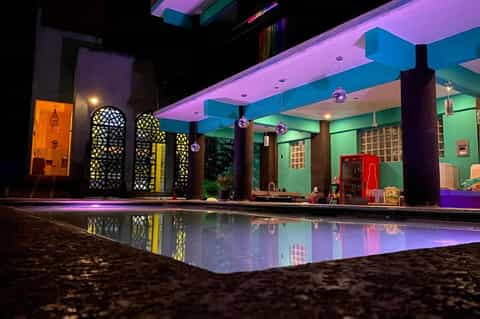 Colorful illuminated resort pool area at night with vibrant pink, blue, and green lighting