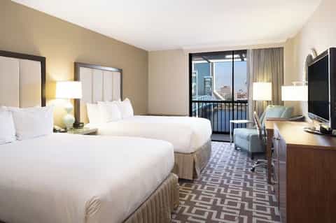 Hotel room with two queen beds, balcony with city view, flat-screen TV, and work desk