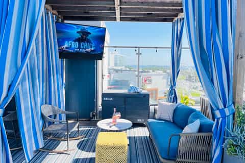 Rooftop lounge with blue striped cabana, modern seating, and city views with entertainment display