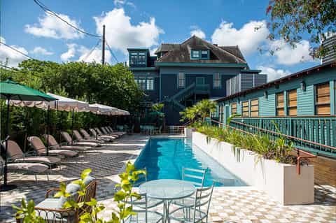 Resort courtyard with lap pool, lounge chairs, teal pergola structure, and historic buildings