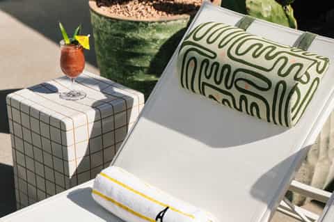Poolside lounge chair with cocktail, book, and decorative potted plant in sunlight