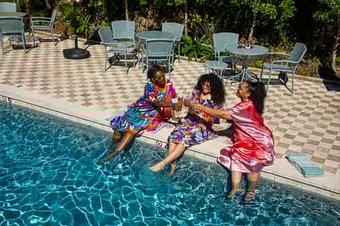 Children playing at the edge of a sparkling swimming pool surrounded by patio furniture and lush landscaping