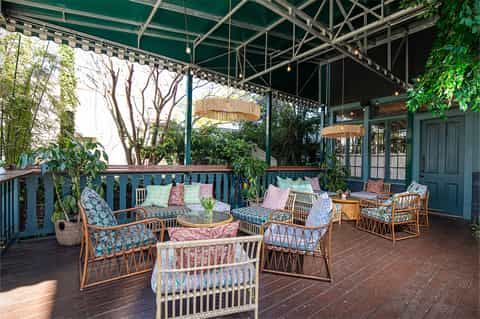 Covered resort patio with wicker lounge chairs, colorful cushions, climbing vines, and lush greenery