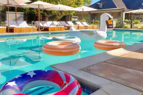 Resort pool with colorful inflatable floats and white lounge chairs under umbrellas