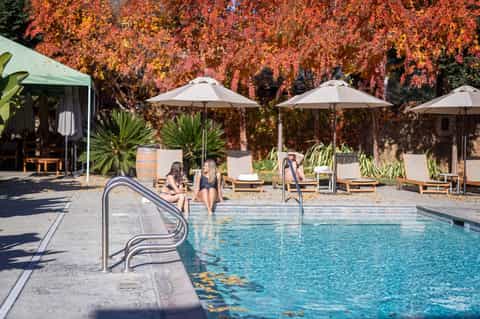 Outdoor pool with white umbrellas, lounge chairs, and red autumn foliage backdrop at resort