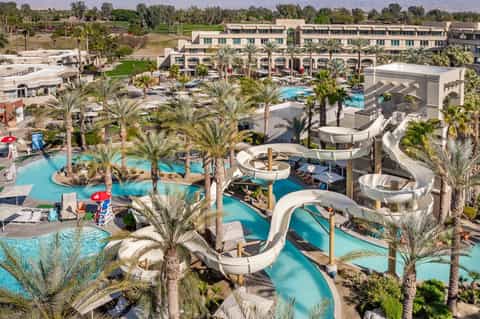 Aerial view of large resort with multiple turquoise pools, water slides, and palm trees