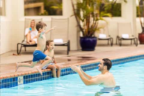 Young child jumping into pool while instructor catches them in shallow water
