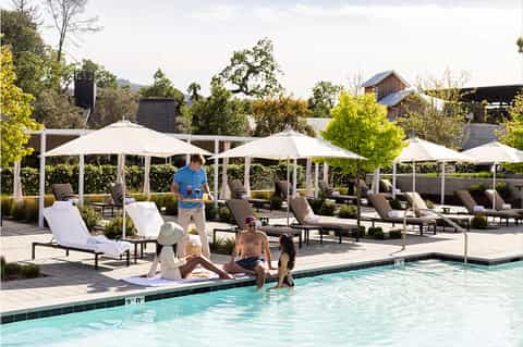 Resort pool area with white umbrellas, lounge chairs, and mountain views