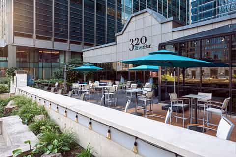 Outdoor RiverBar patio with turquoise umbrellas, modern seating, and urban building backdrop