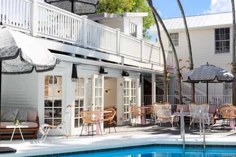 Waterfront resort deck with dining area, wicker chairs, pool, and palm trees