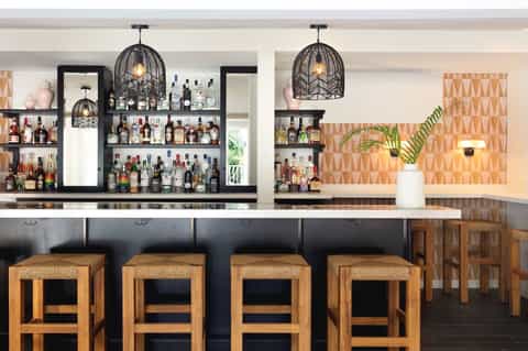 Upscale bar with black birdcage pendant lights, geometric wallpaper, and wooden bar stools