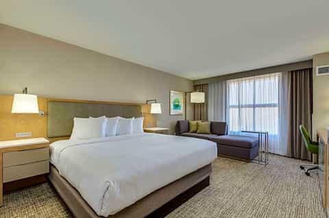Hotel bedroom with king bed, sofa seating area, and balcony overlooking the resort
