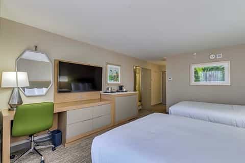 Hotel room with two queen beds, flat-screen TV, desk with green chair, and bathroom